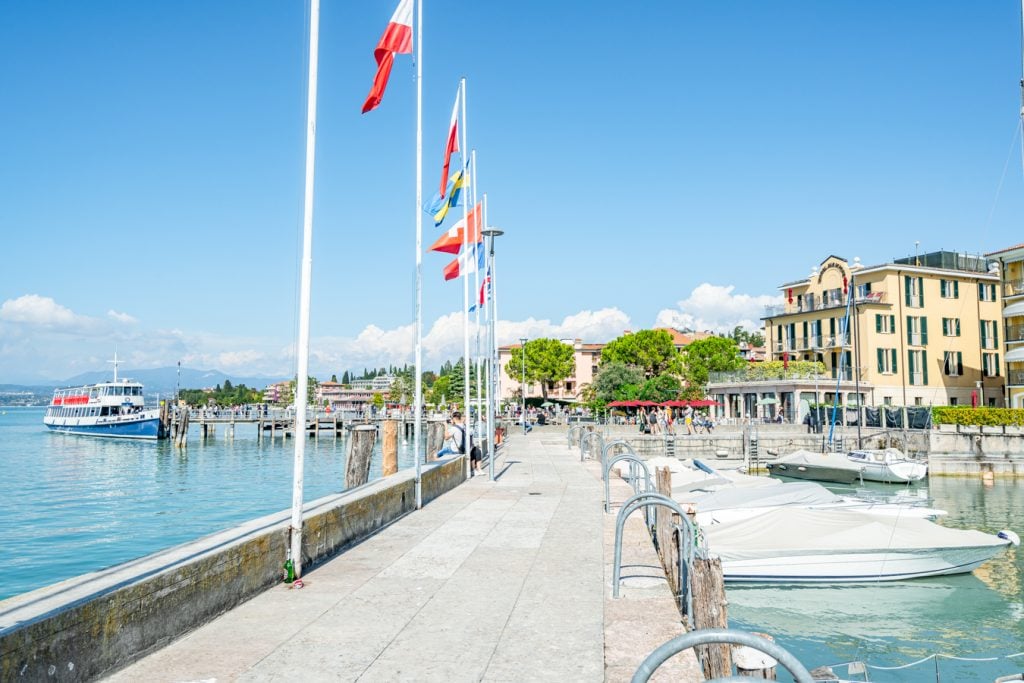 Promenade along the water in Sirmione, Lake Garda, with flags on the left side