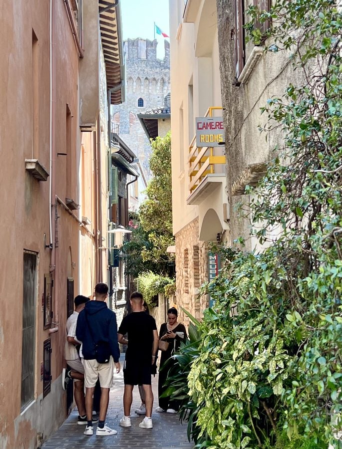 Group of people enjoying a narrow street in Sirmione with the castle tower in the distance