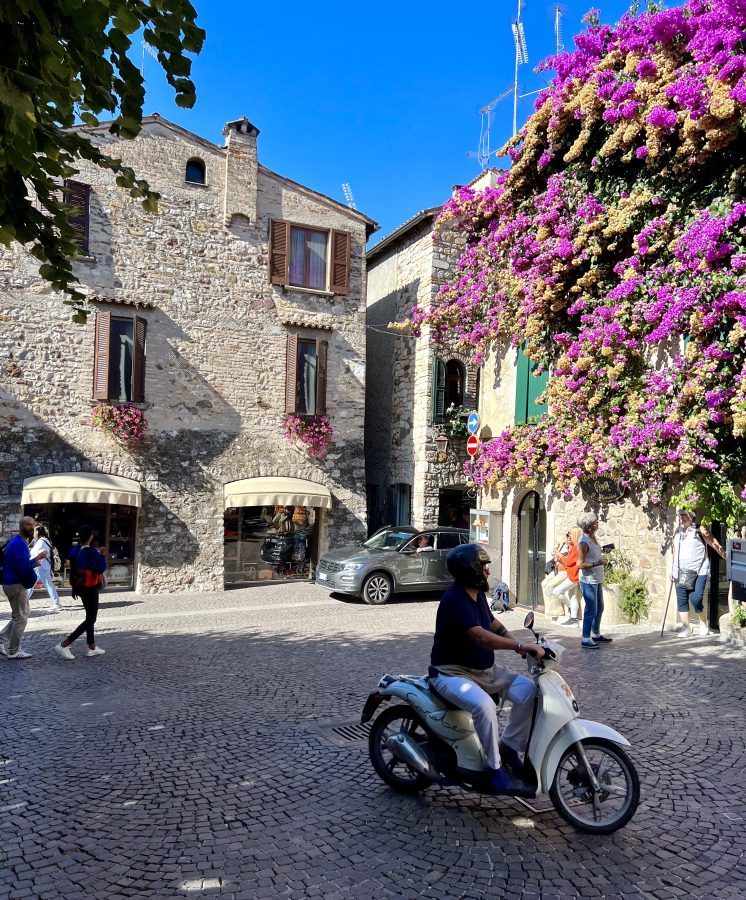 Motorbike crossing through a piazza in Sirmione with blooming bougainvillea in the backdrop