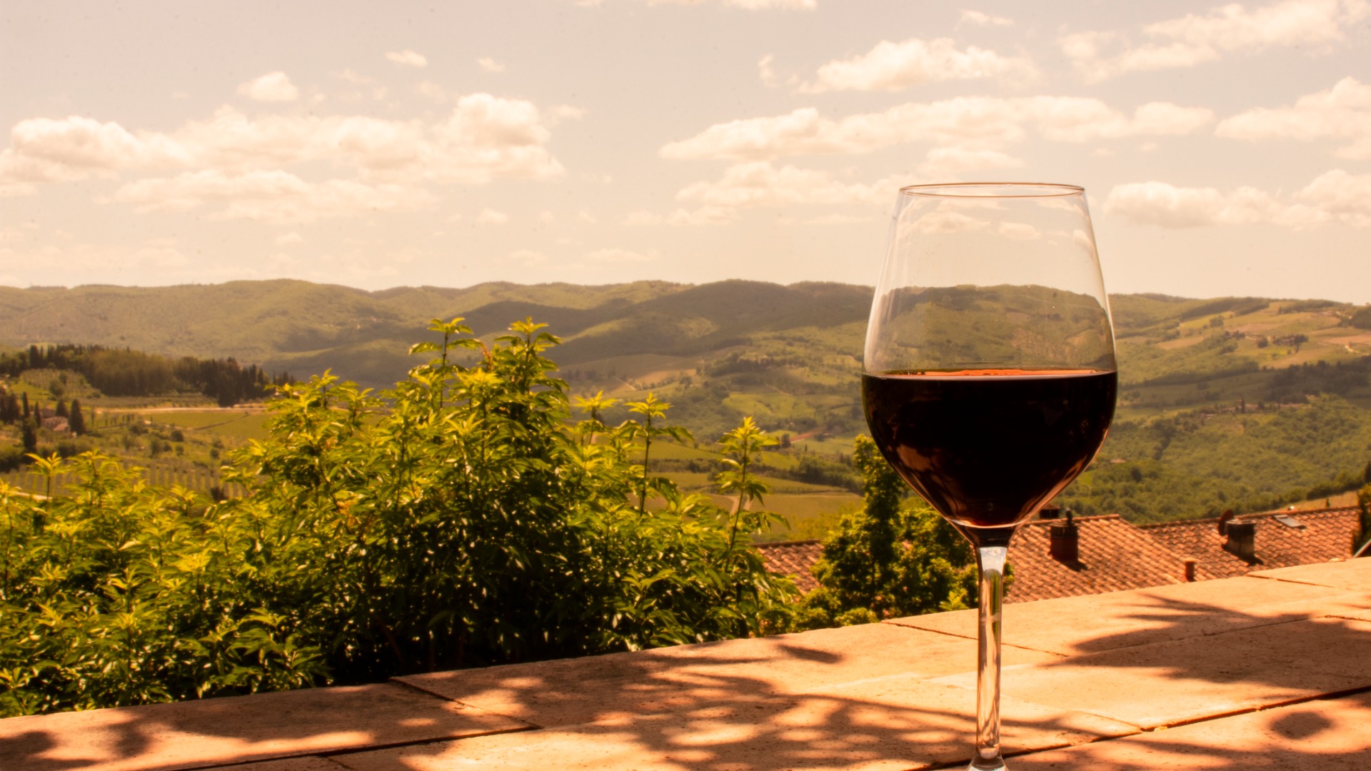 A glass of red wine in the foreground with the rolling hills of Tuscany in the background.