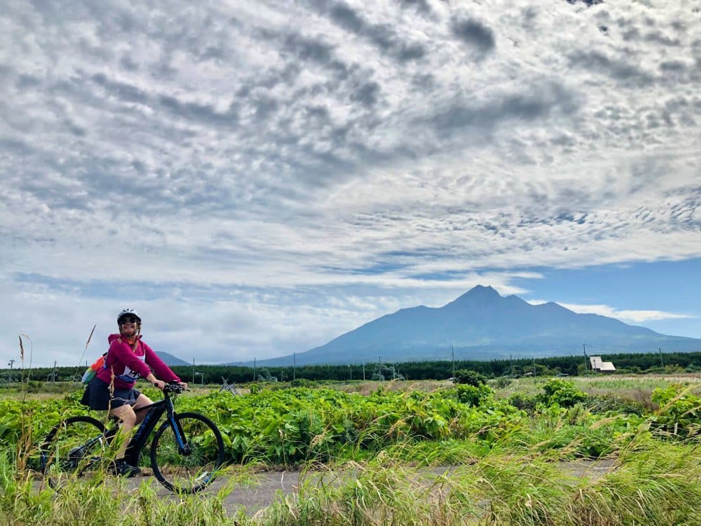 A woman cycling in Rishiri Island with Mount Rishiri in the background