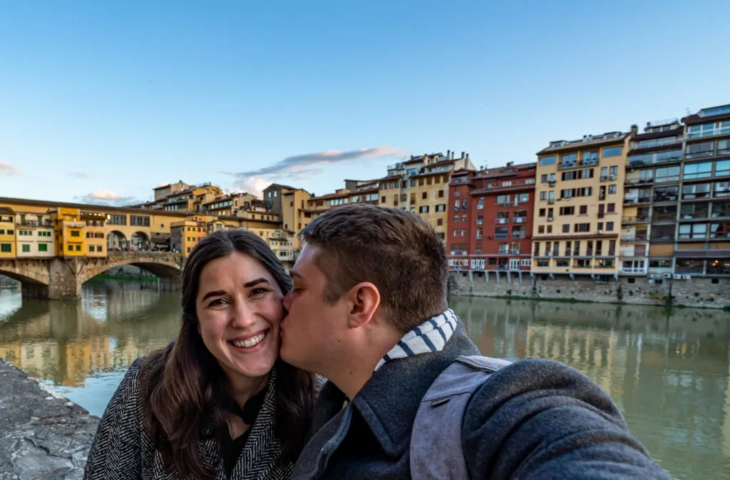 Kate Storm and Jeremy Storm sitting by the Arno with the Ponte Vecchio in the background