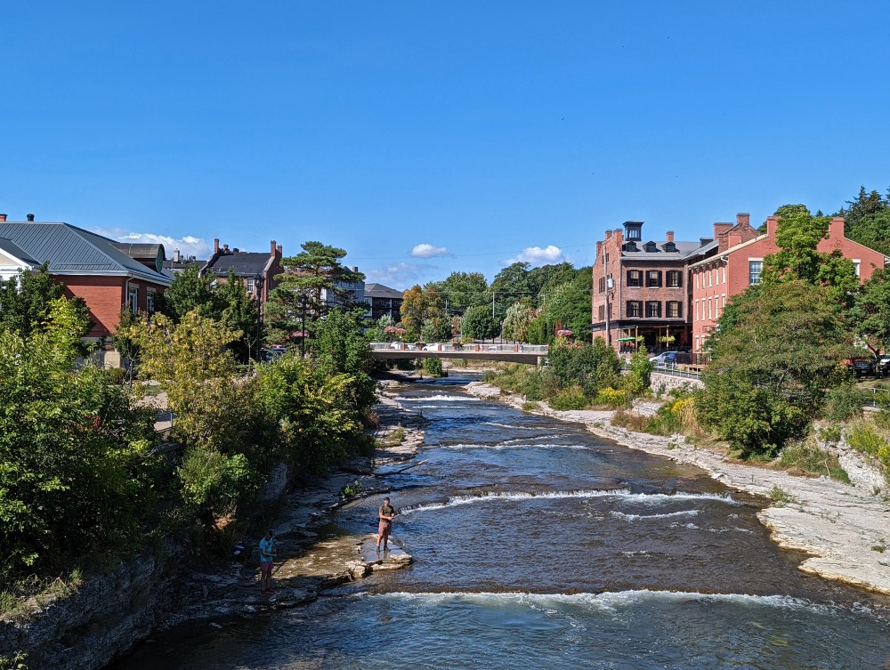 Ganaraska River in Port Hope that's flanked by trees and has a bridge and historic buildings in the distance along its banks