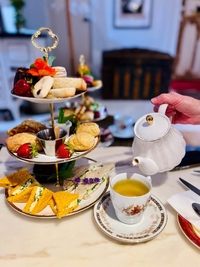 lady pouring tea with tiers of sandwiches and treats