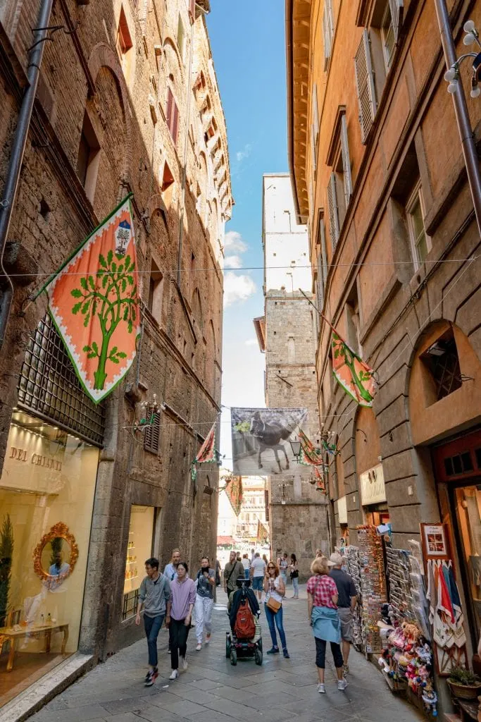 Narrow street in Siena, Italy decorated with contrade flags, a charming stop during a 3-day Tuscany itinerary