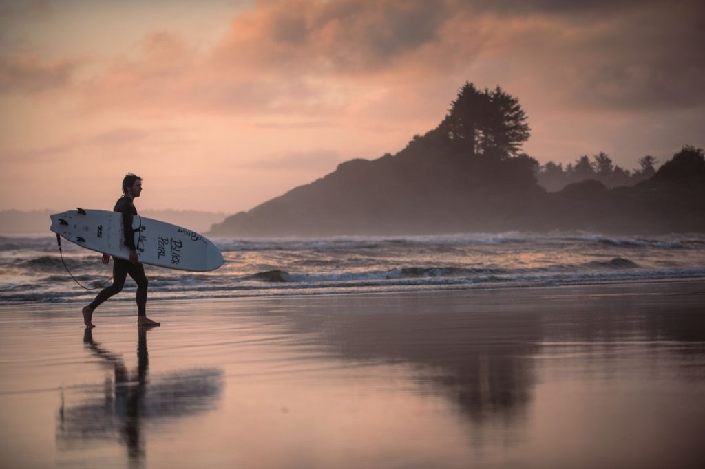 A surfer on the beach in Cox Bay, Tofino, British Columbia. Image credit: Destination Canada / Brian Caissie