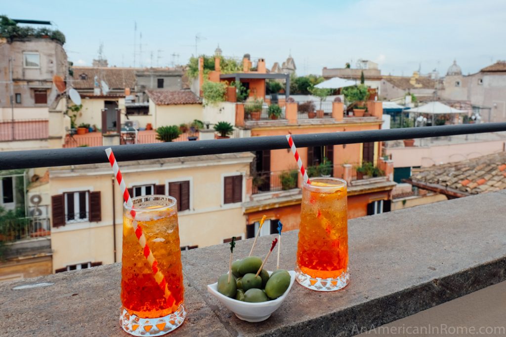 Two red spritz cocktails on a rooftop in Rome with a bowl of olives