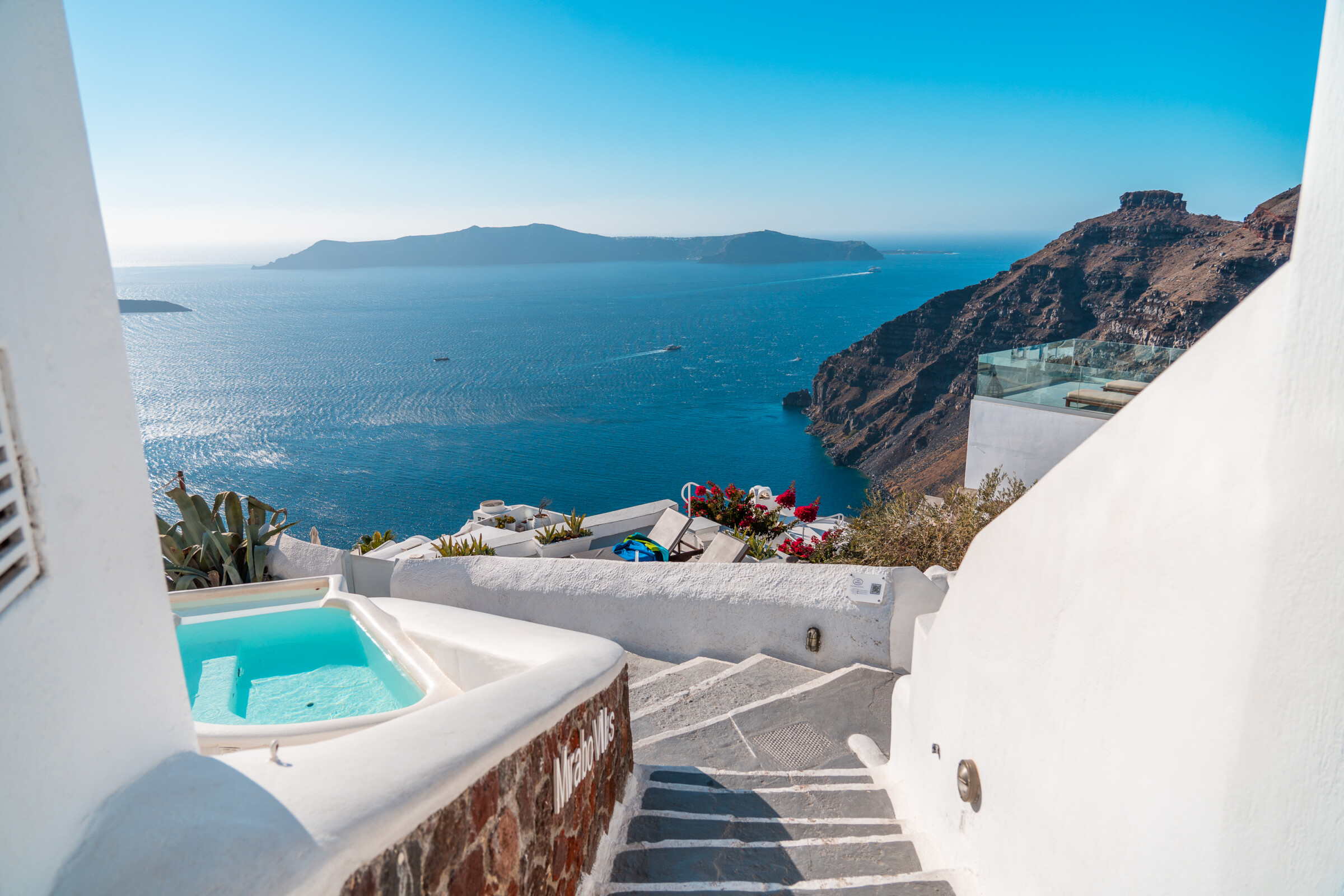 Whitewashed stairs and a small pool in Santorini, with the iconic Skaros Rock in the background.