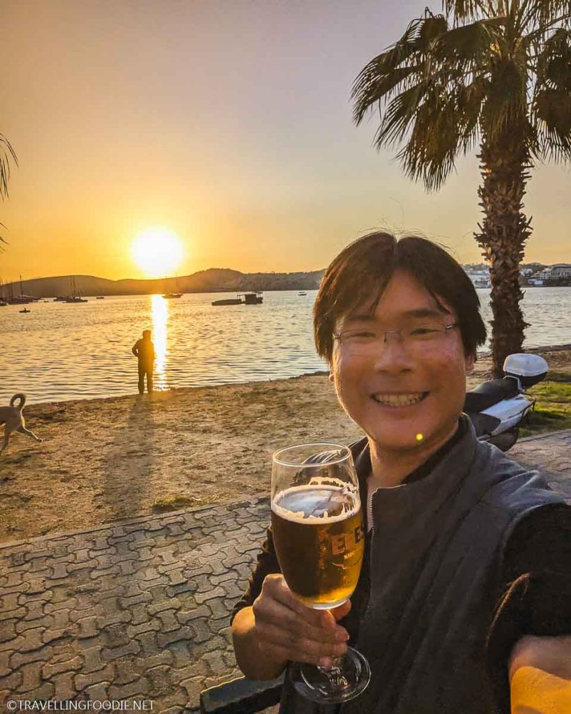 Travelling Foodie Raymond Cua holding beer during sunset at Gumbet Cafe