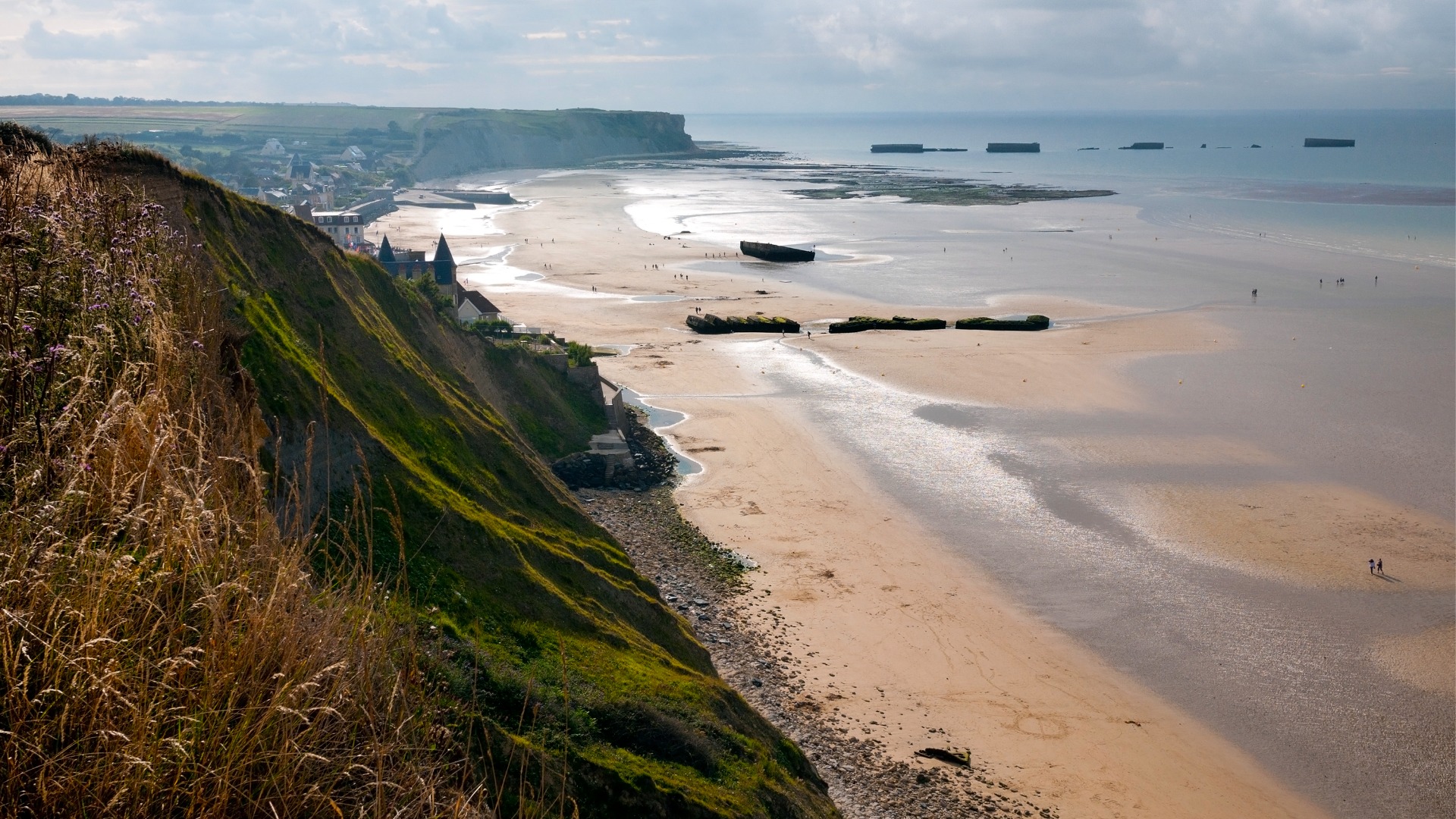 This is a panoramic view of a beach in Normandy. There are green cliffs going down to the white sand.