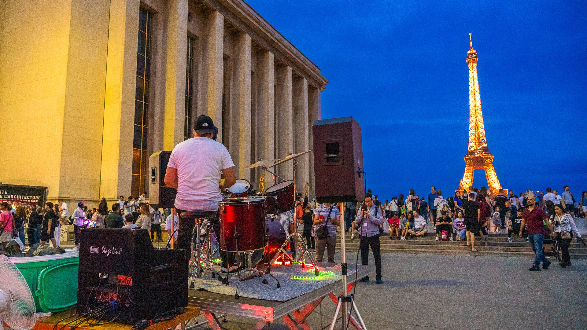 This image shows a band performing with an audience watching. The illuminated Eiffel Tower is in the background.