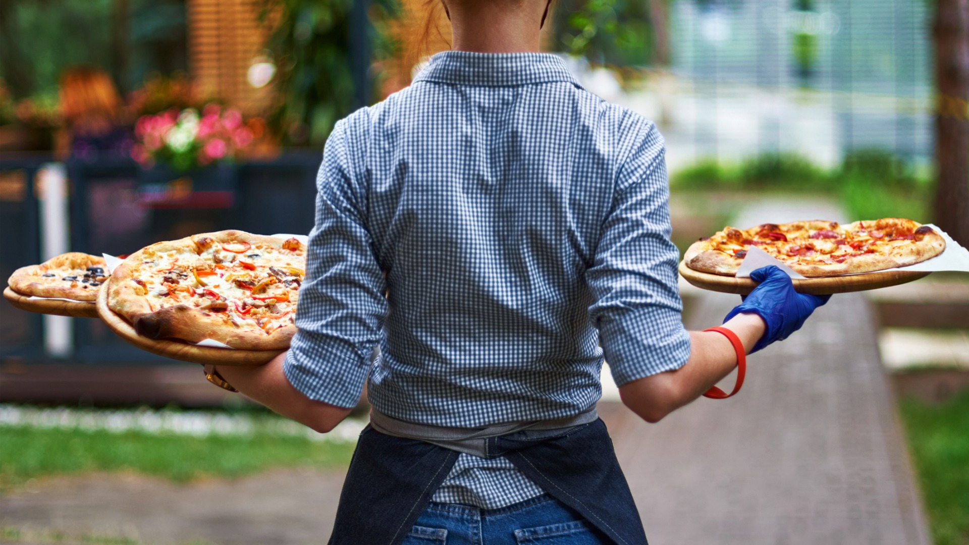 This image shows a female server with her back turned to the camera, holding three large pizzas. The tipping culture in Europe dictates that good servers should be rewarded for their skills.