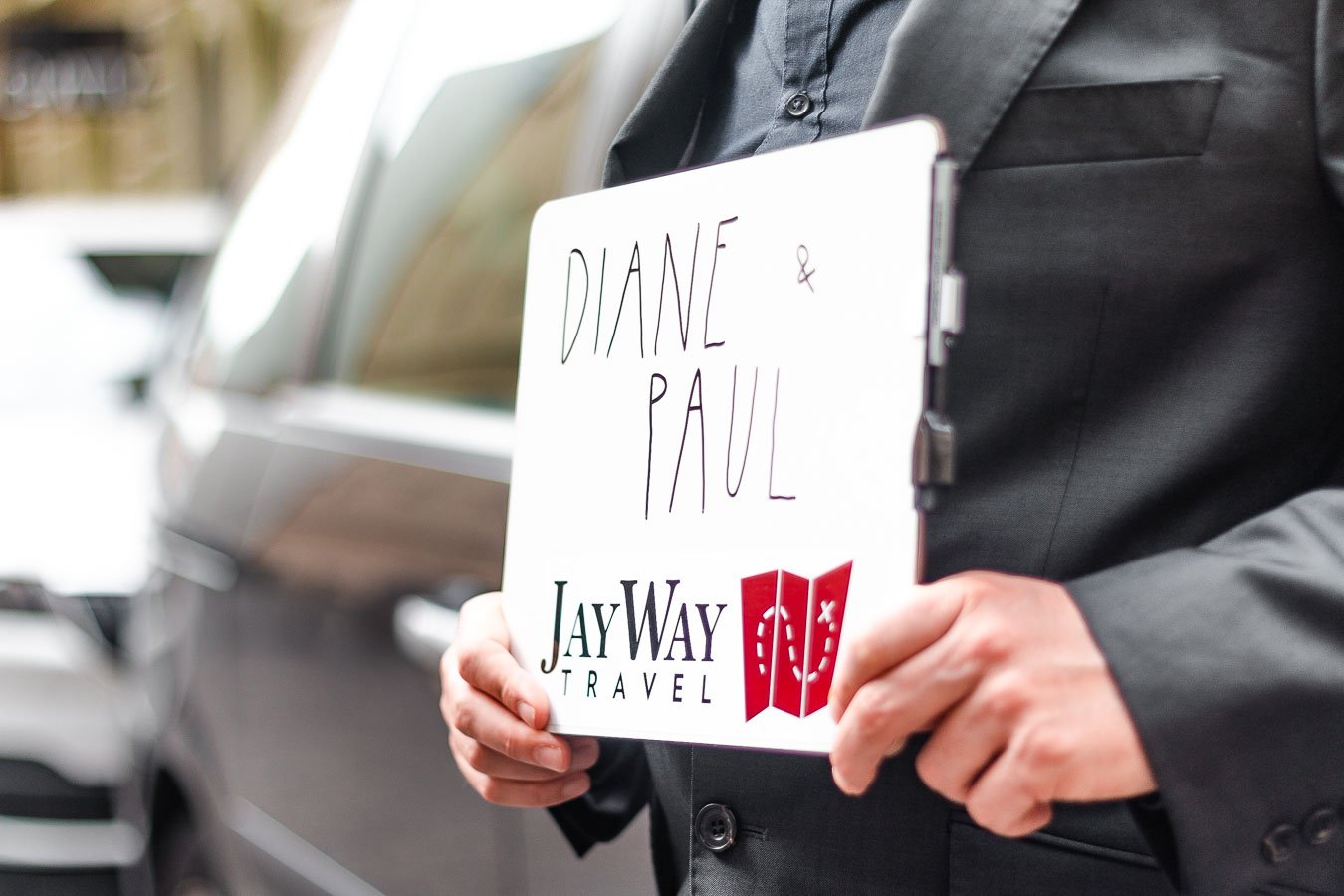 This is a close-up of a man holding a JayWay Travel sign with the names Diane & Paul written on it.