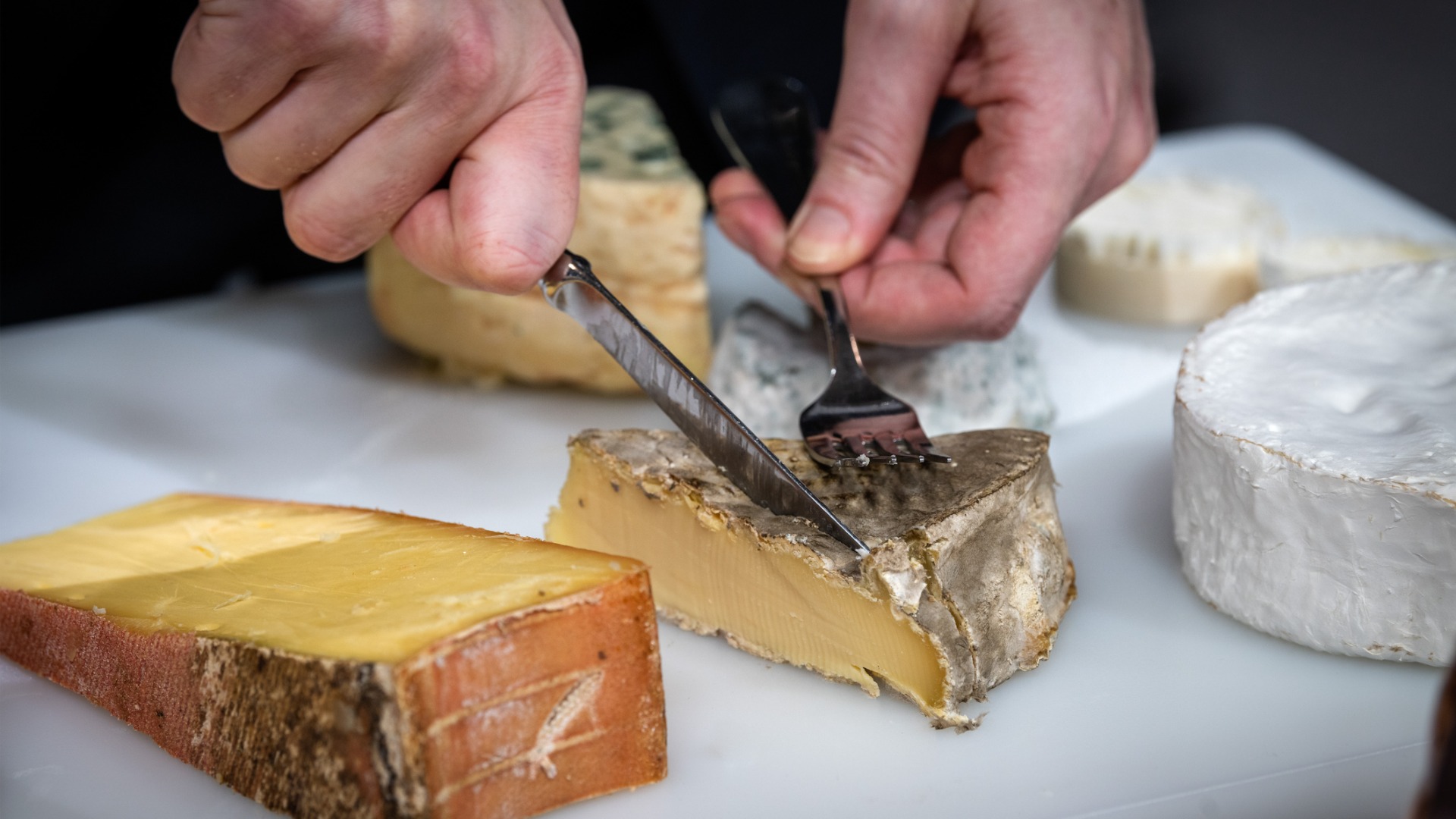 This is a close-up of a man cutting cheese in a platter of various types of French cheese.