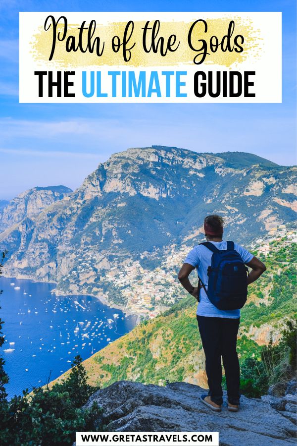 Photo of a guy in a white t-shirt and shorts standing in front of Positano and the Amalfi Coastline with text overlay saying 'Path of the Gods Ultimate Guide'