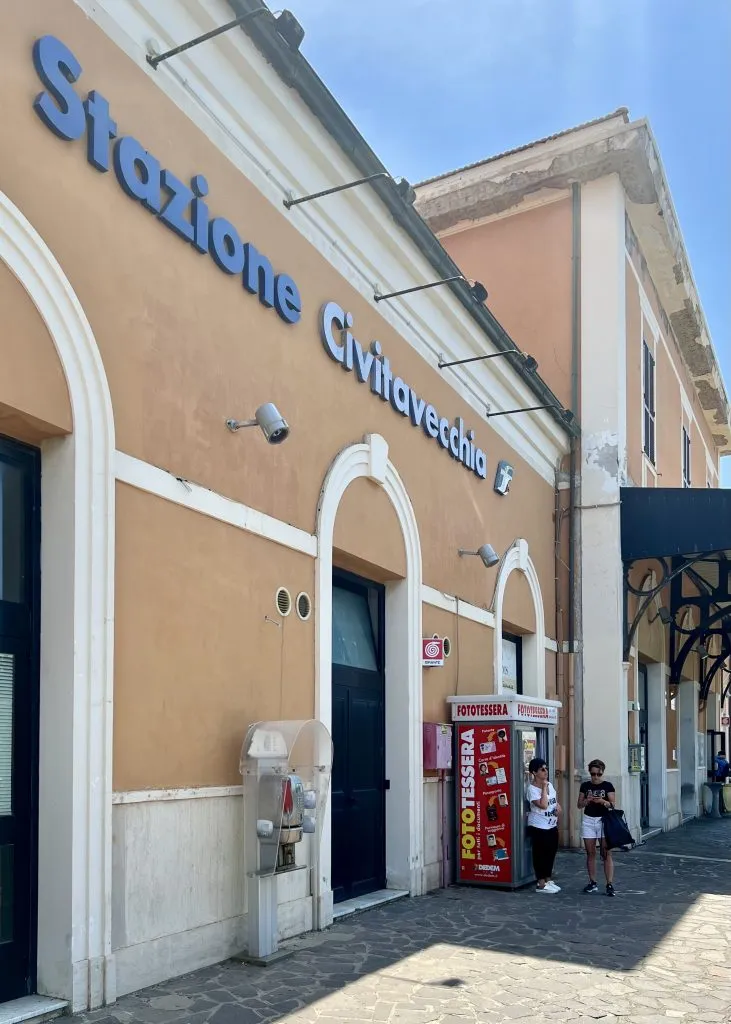 Front facade of the Civitavecchia train station, a yellow building with "Stazione Civitavecchia" written in blue