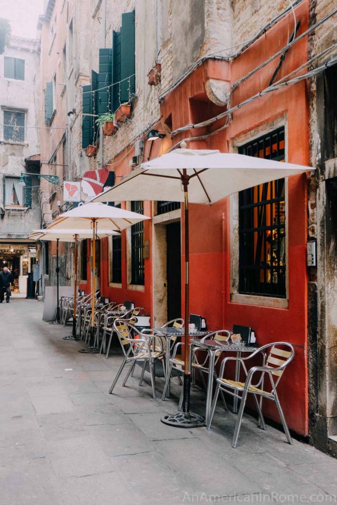 Exterior of Caffé del Doge in Venice, with orange walls and white umbrellas over outdoor tables