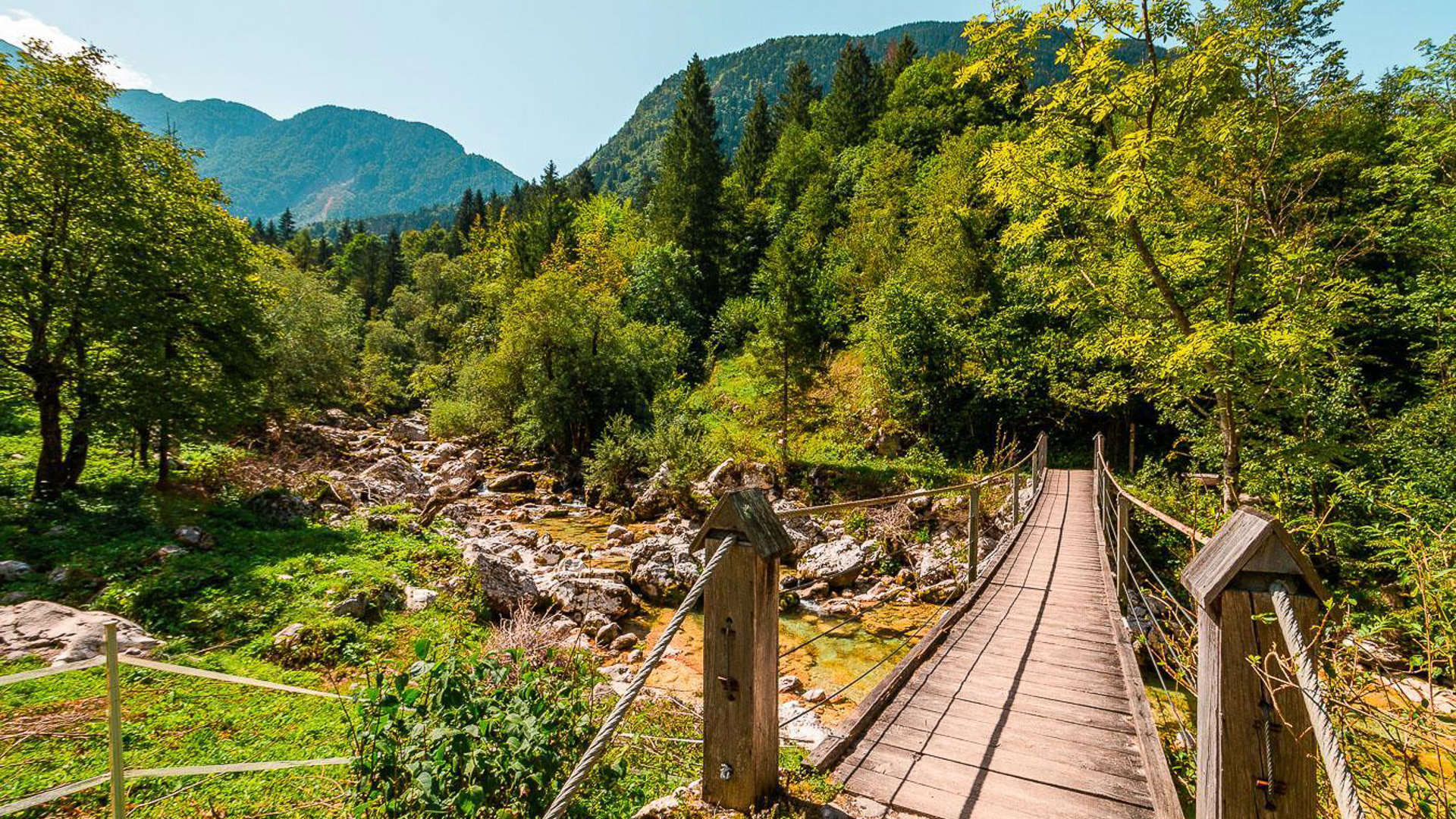 A picturesque view of Soca Valley national park featuring a wooden suspension bridge and majestic mountains.