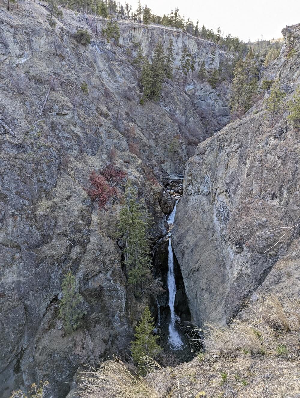 Looking up at a thin triple-level waterfall on the side of a rocky canyon