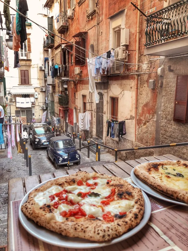 Two traditional Napoli-style pizzas on a small street in Naples