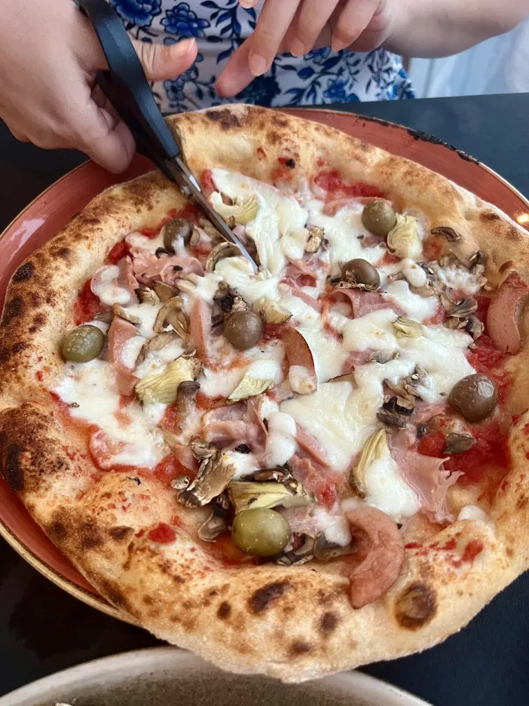 Kate Storm slicing a traditional Capricciosa pizza with scissors