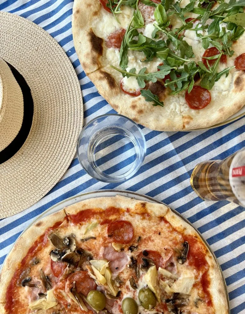 Flat lay of two pizzas in an Italian restaurant with a sunhat and beer