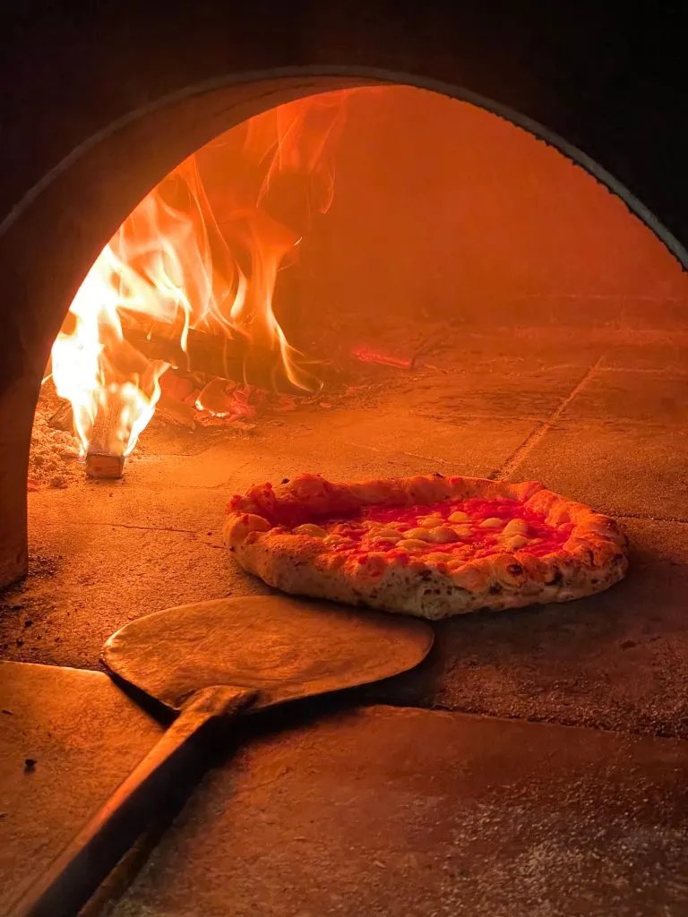 Close-up of a pizza in Italy with a paddle nearby in a wood-burning pizza oven