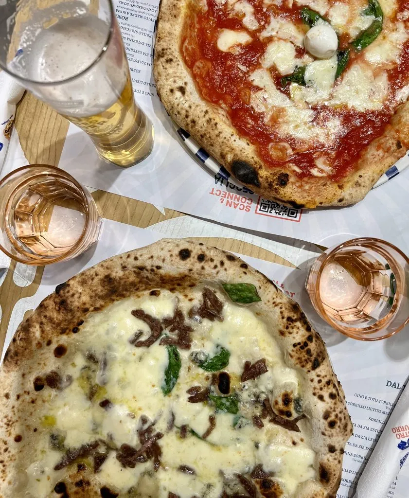 Two Neapolitan-style pizzas arranged on a table with beer