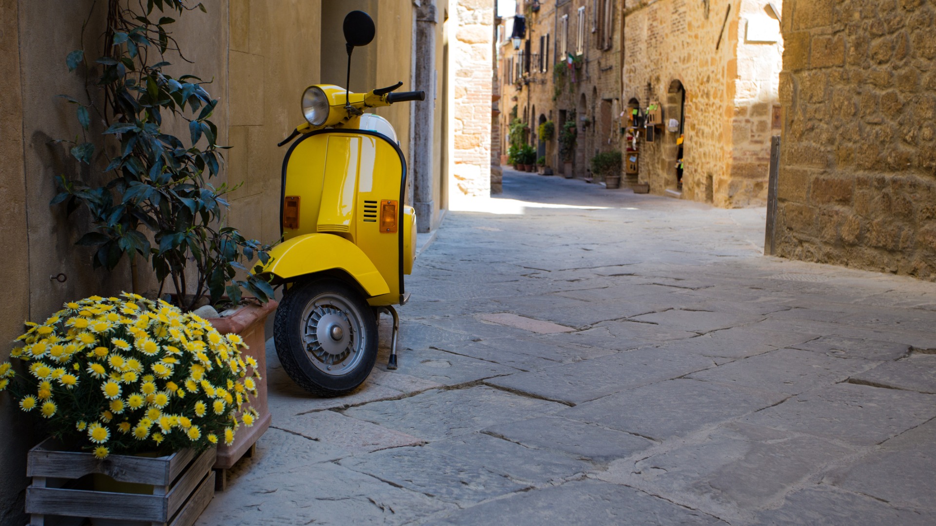 A yellow vintage Vespa parked in a charming street in Italy.