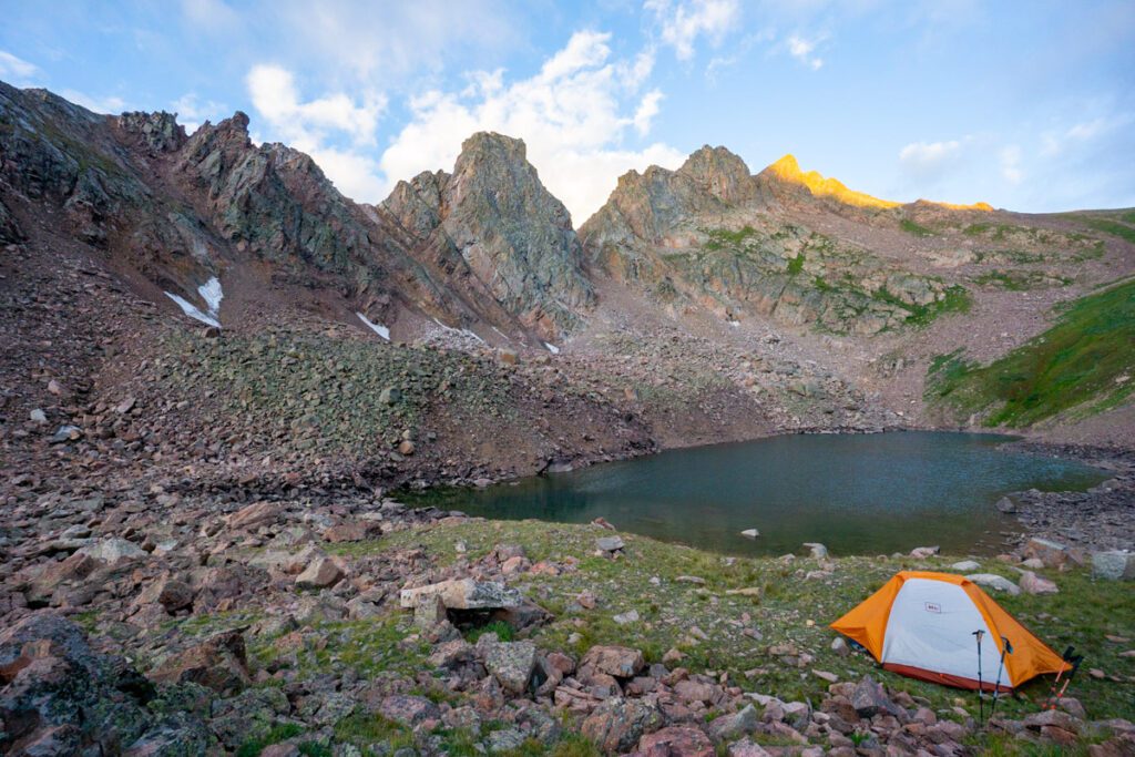 A backpacking tent set up near a mountain lake during sunset.