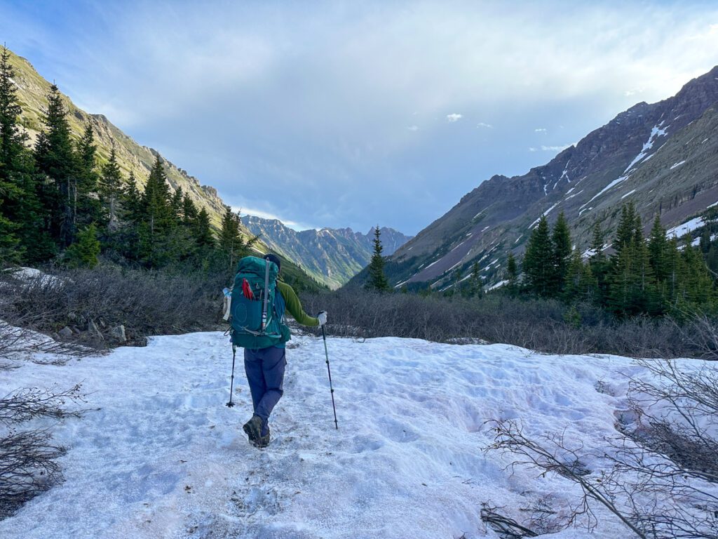 A person crossing a snowfield while carrying a large backpack in the mountains.