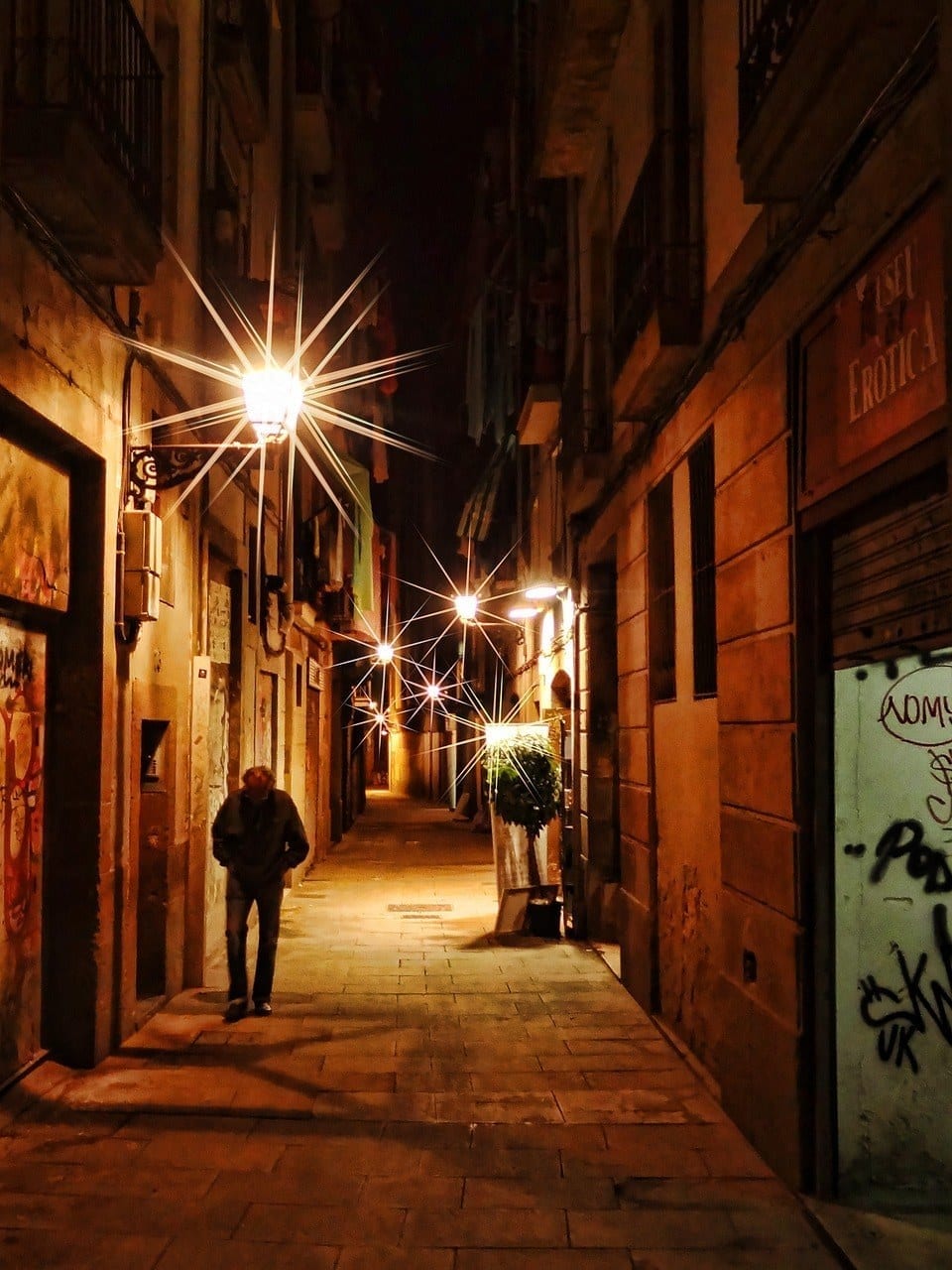 A quaint, tree-lined side street in El Born, Barcelona; street lamps resembling stars illuminate the narrow path.