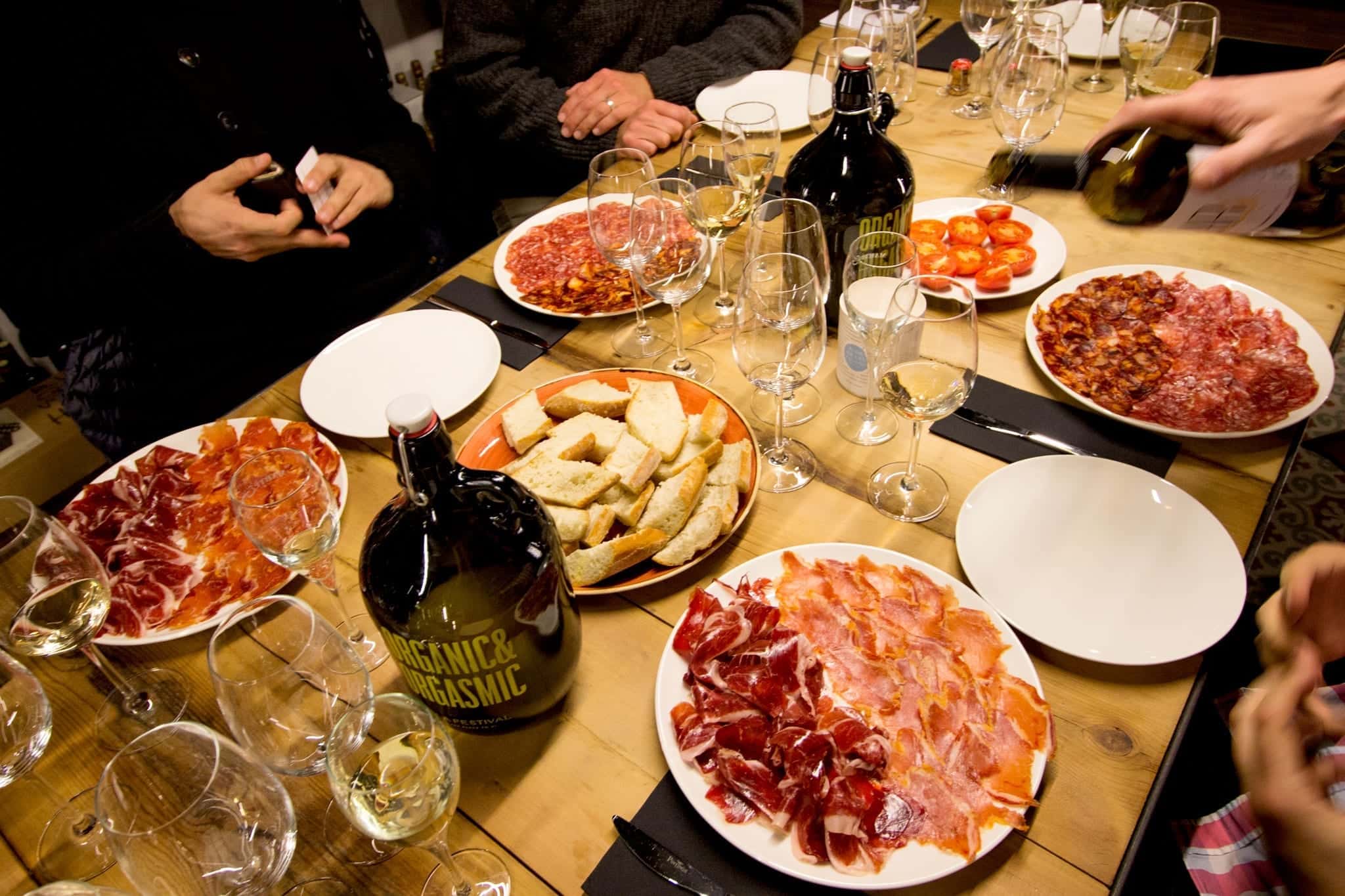 A table laid out with tapas and wine glasses, while a hand pours from a bottle.