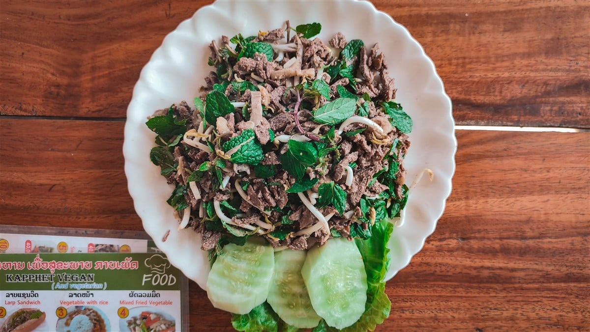 Plate of Laap, a traditional Laotian dish, featuring minced meat mixed with fresh herbs and vegetables, served on a white plate with cucumber slices.