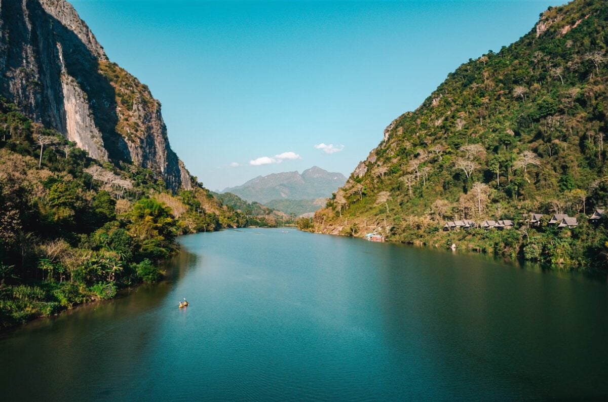 Kayaking on the Nam Ou River in Nong Khiaw surrounded by towering green cliffs and a clear blue sky