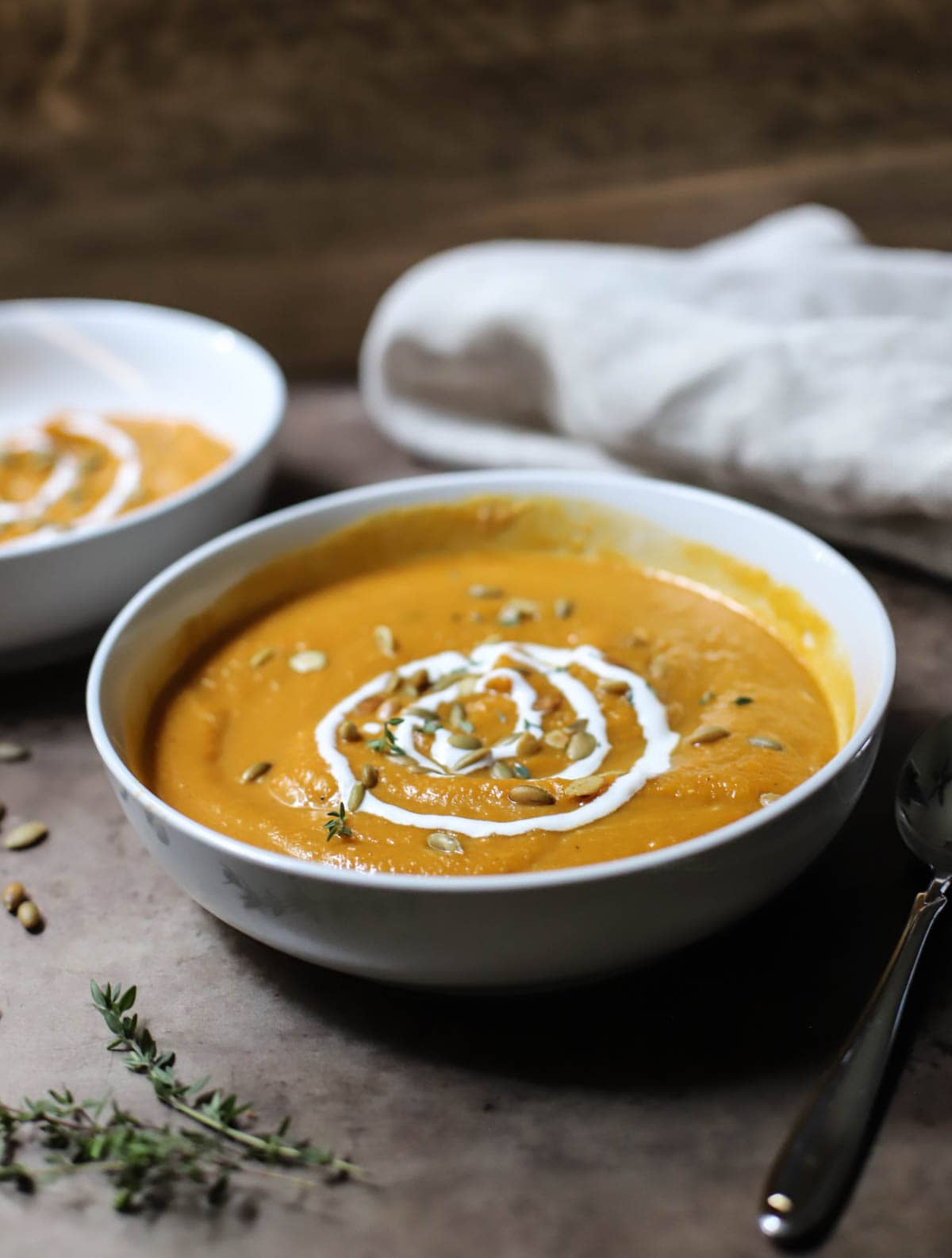 Butternut squash soup garnished with sour cream and pepitas served in a white bowl on a wooden counter.