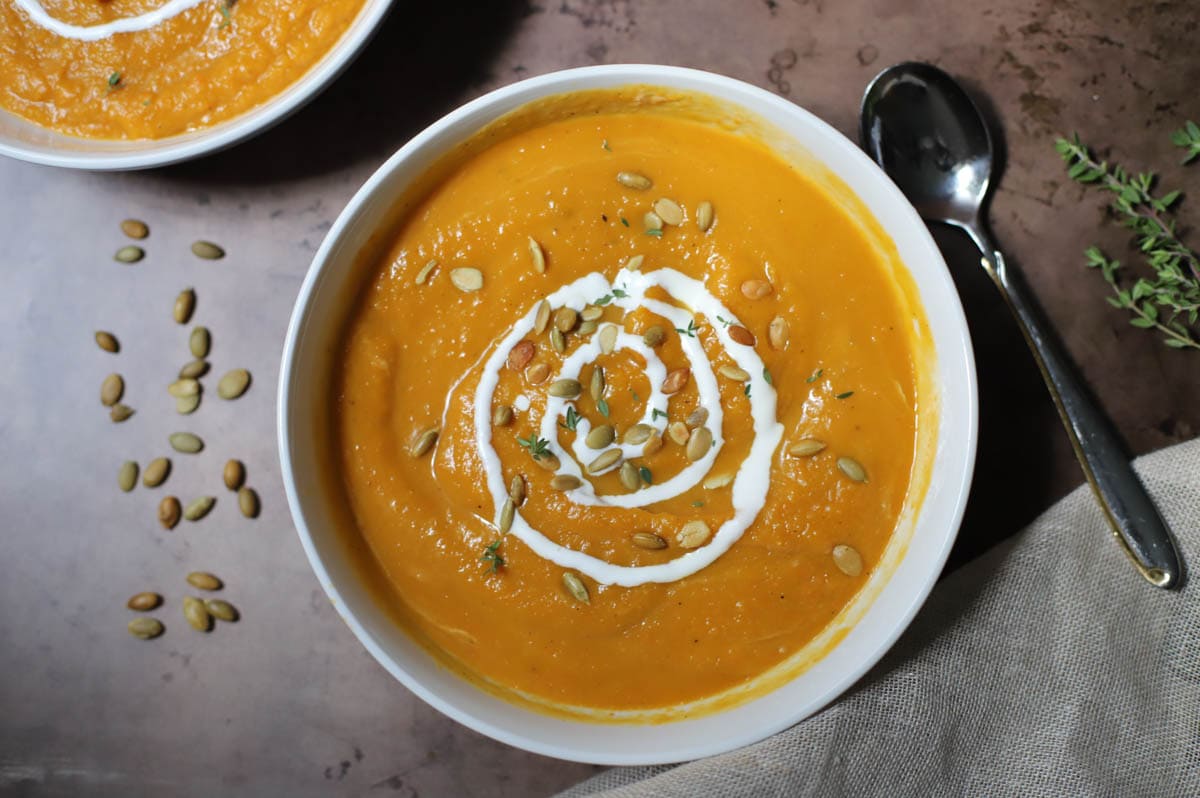 Final butternut squash soup served in a bowl with sour cream and pepitas.