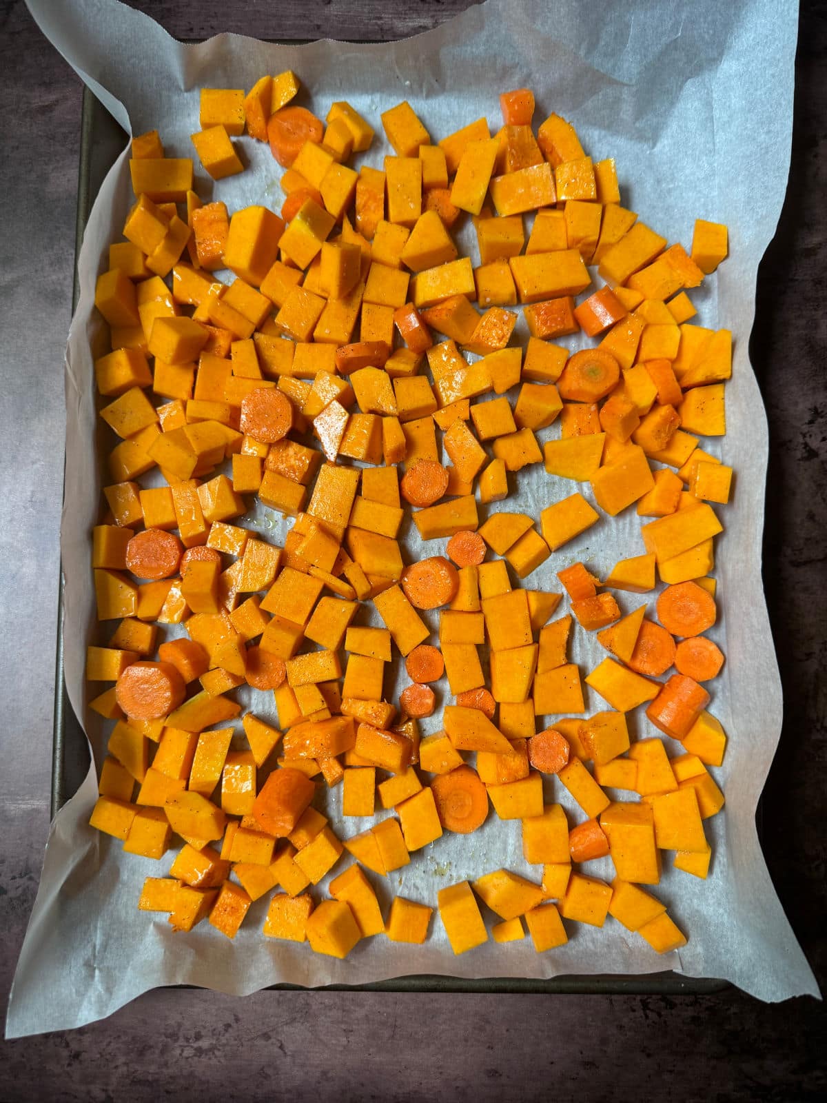 Cubed butternut squash spread out on parchment paper on a baking sheet.