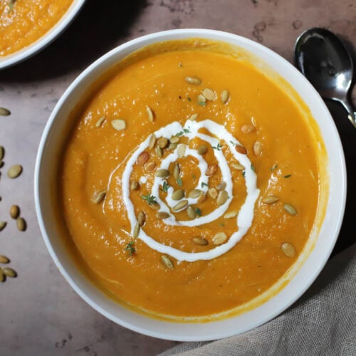 Butternut squash soup garnished with sour cream and pepitas in a bowl.