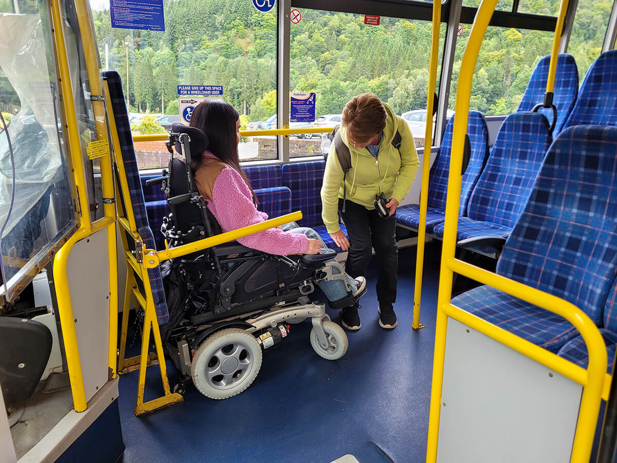 Emma seated in the wheelchair space on the bus with her mother next to her.