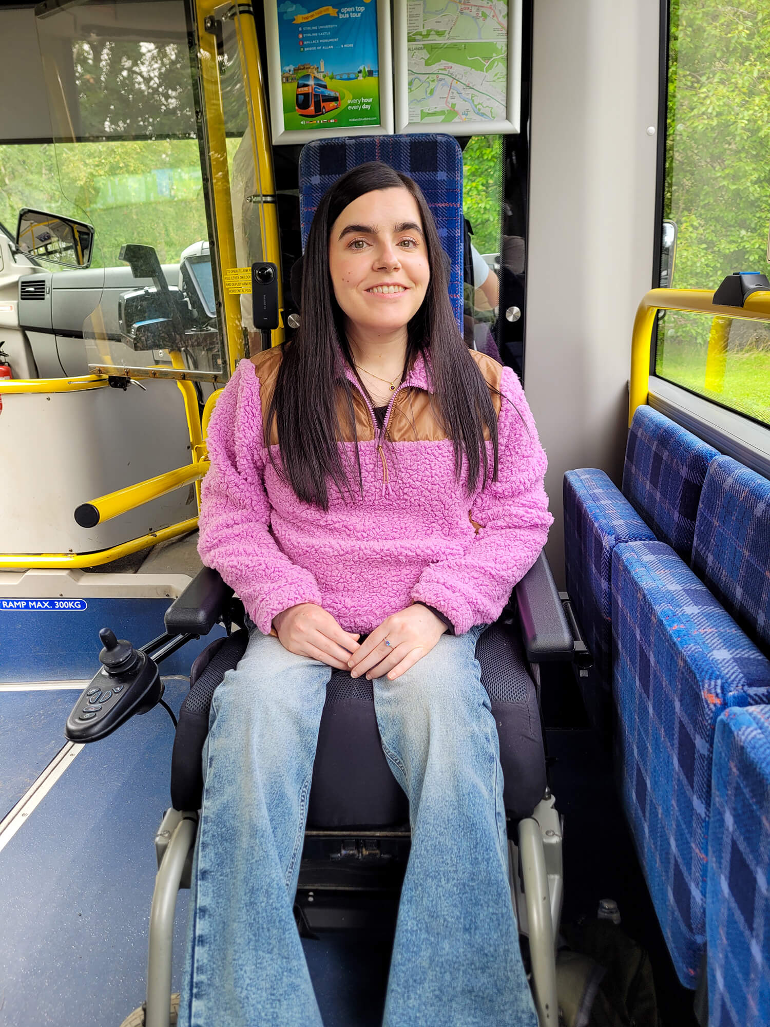 Emma sitting in her wheelchair on the bus, smiling at the camera.