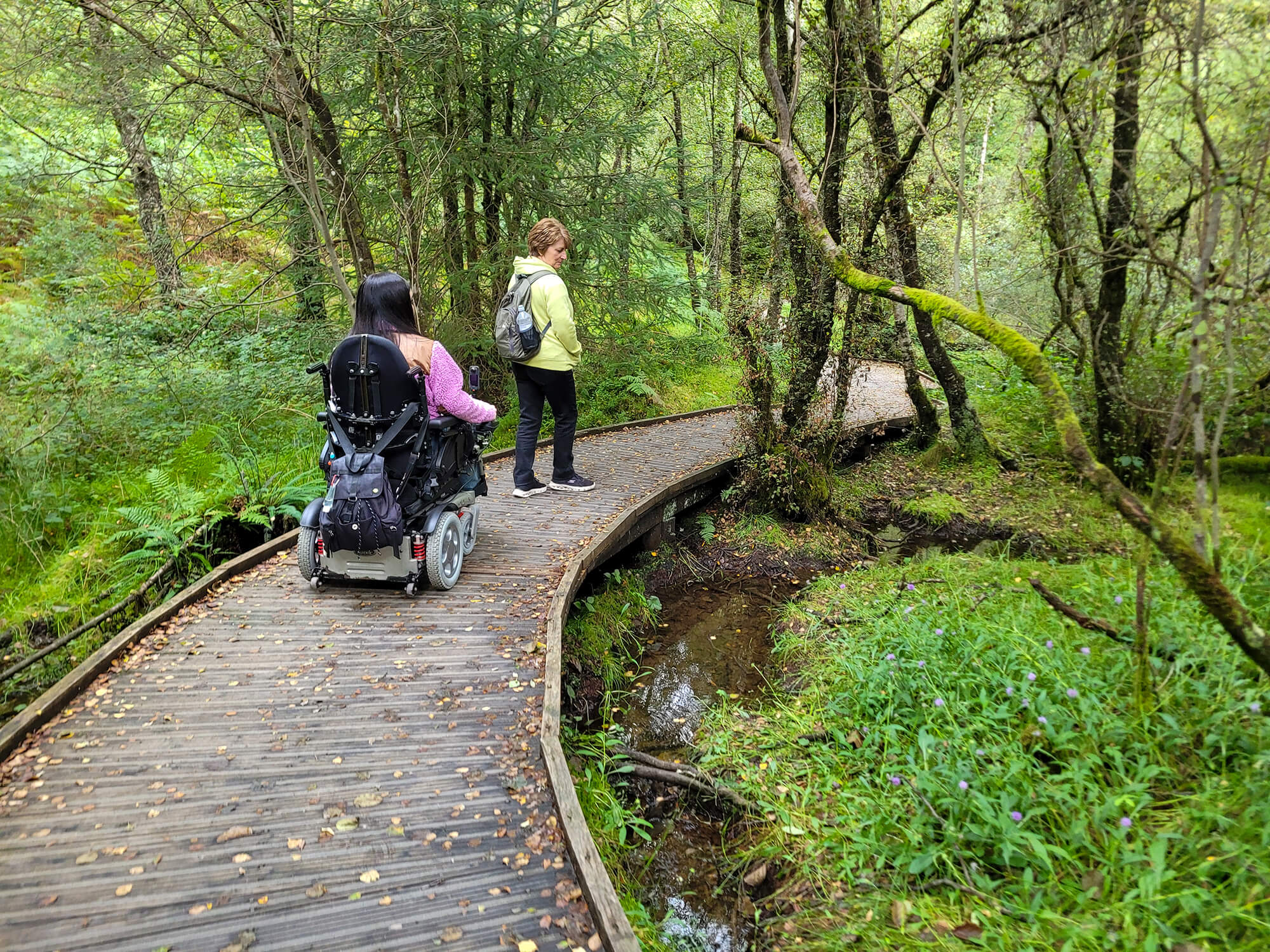 Emma driving her wheelchair across a wooden walkway on the Waterfall Trail at The Lodge in the Queen Elizabeth Forest, Aberfoyle.