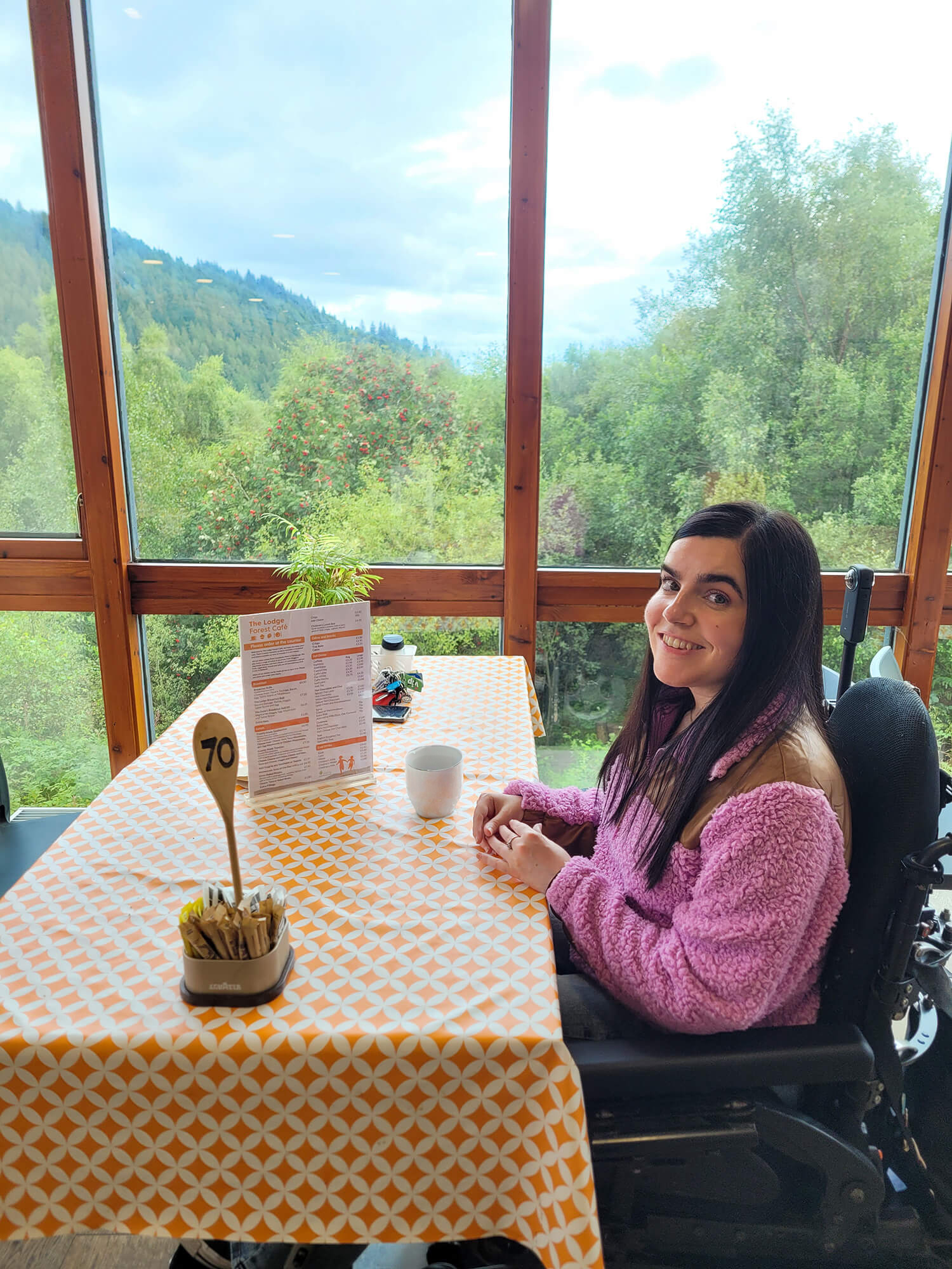 Emma seated at a table in The Lodge Forest Cafe, enjoying views across Queen Elizabeth Forest Park.