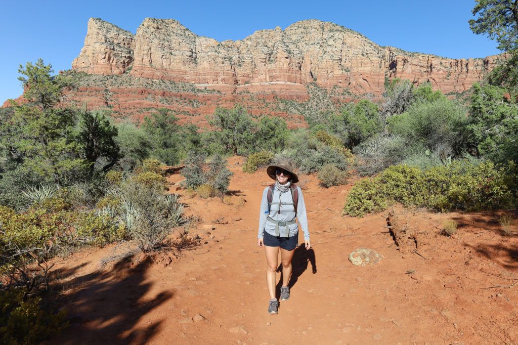 Woman hiking on red rock dirt path in Sedona with red and white bluffs behind her