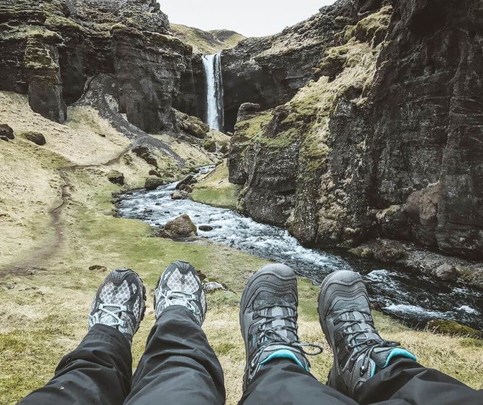 Jeannie and her husband showcasing their hiking boots as part of their rain gear for Iceland near Kvernufoss Waterfall | Iceland with a View