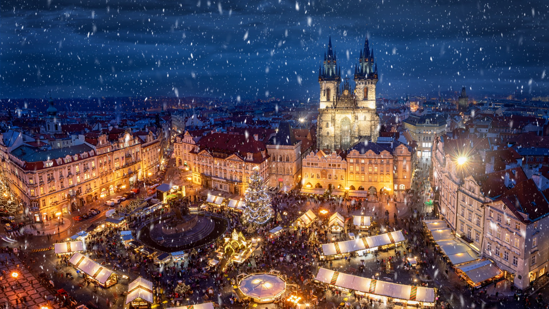 An aerial view of the Old Town Square Christmas Market in Prague, bustling with people on a snowy evening.