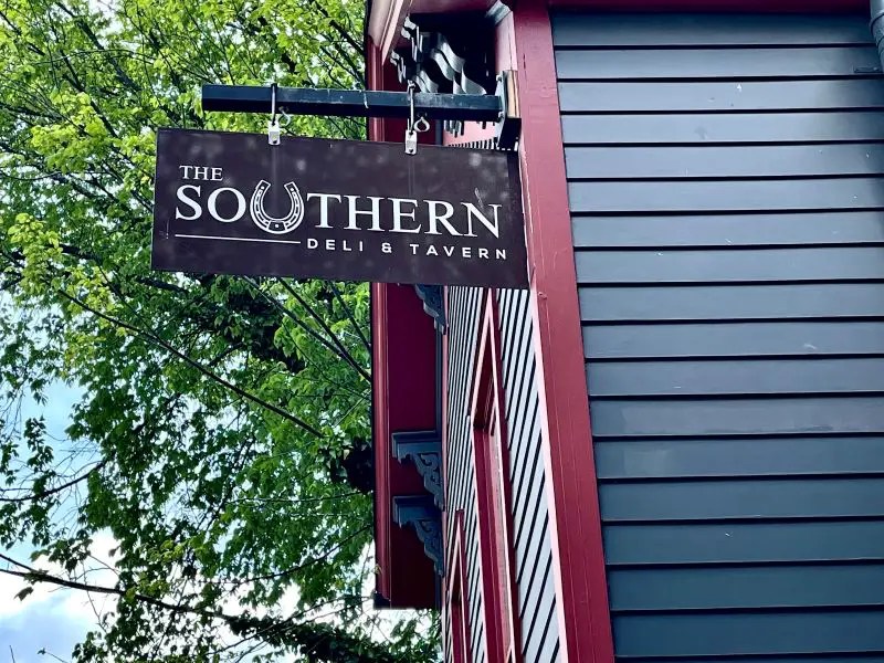 Historic house in downtown Lexington with navy siding and gingerbread trim. A sign hangs in front for the restaurant - The Southern Deli & Tavern, one of the stops on the Downtown Lexington Food Tour offered by Bites of the Bluegrass.