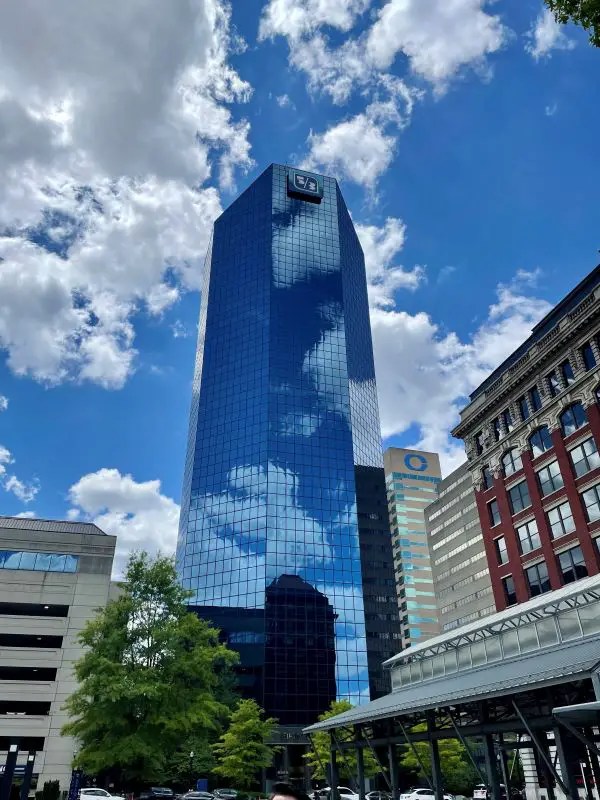 Downtown Lexington skyline include a large blue building soaring into white clouds against a blue sky.