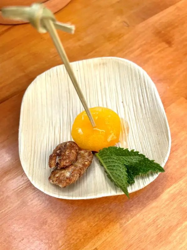 Small wood plate with a glazed apricot, candied pecans and a sprig of mint. One of the food options available when visiting the popular downtown Lexington bar The Grove.