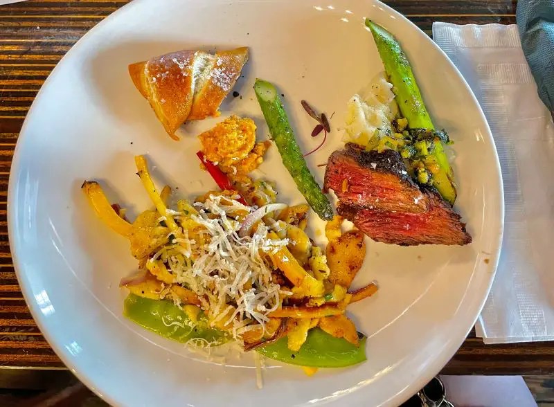 A white plate with a variety of foods including spatzle, hanger steak, asparagus, and part of a pretzel. A sampling of the food available at Salt & Vinegar located inside the Ethereal Public House in downtown Lexington.